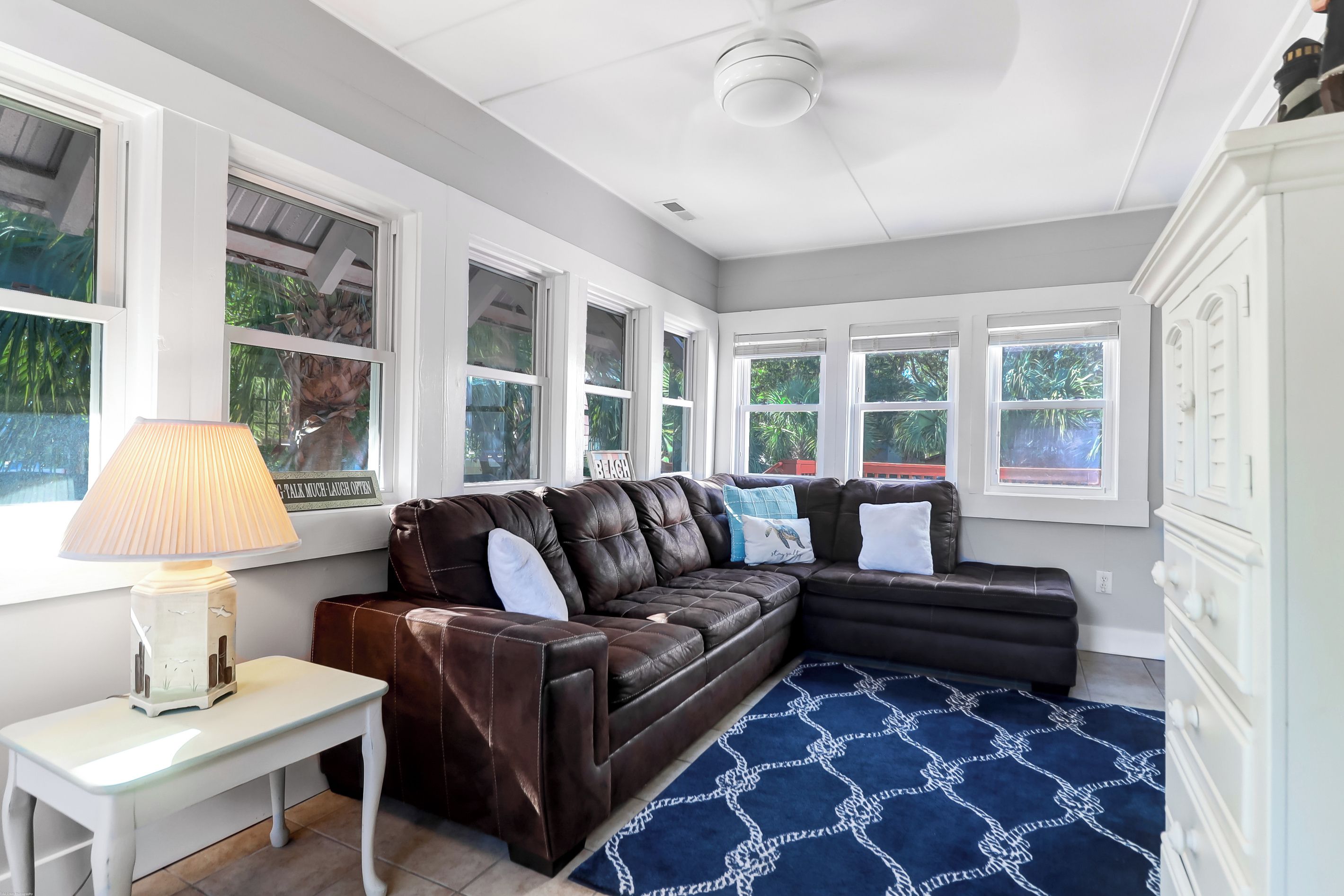 A living room with a brown leather sofa, a small white table with a lamp, and a blue patterned rug.