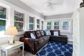 A living room with a brown leather sofa, a small white table with a lamp, and a blue patterned rug.