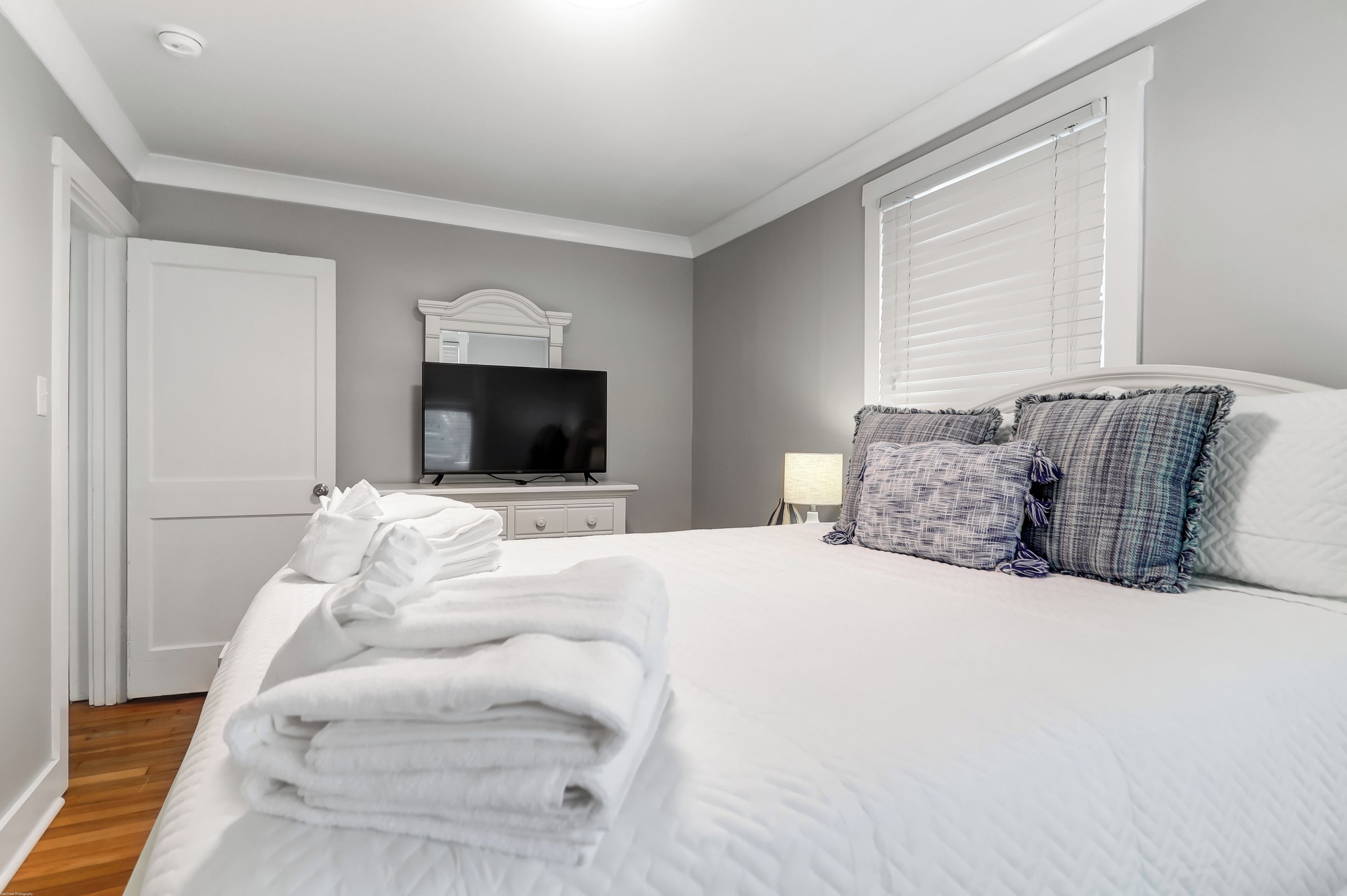 A hotel room with a bed, a television, a bedside table, and a window with blinds.