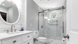 Et moderne badeværelse med et hvidt toiletbord, et rundt spejl, et toilet og et bruseområde med glasvægge.