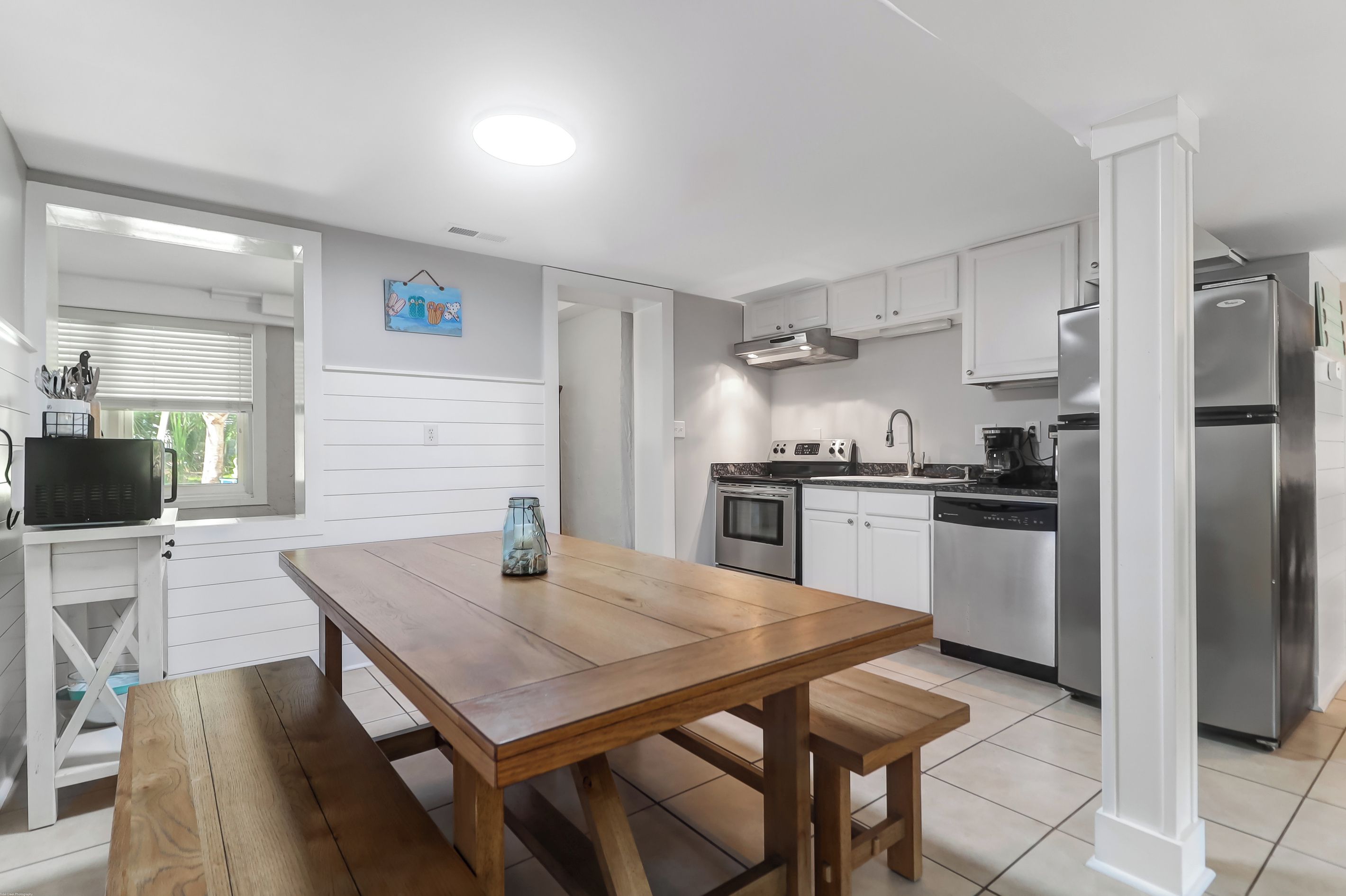 A modern kitchen with white cabinets, stainless steel appliances, and a wooden dining table.