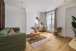 A living room with a green sofa, a round wicker table with a vase, and a wooden floor. - One-Bedroom Superior Apartment (Paris)