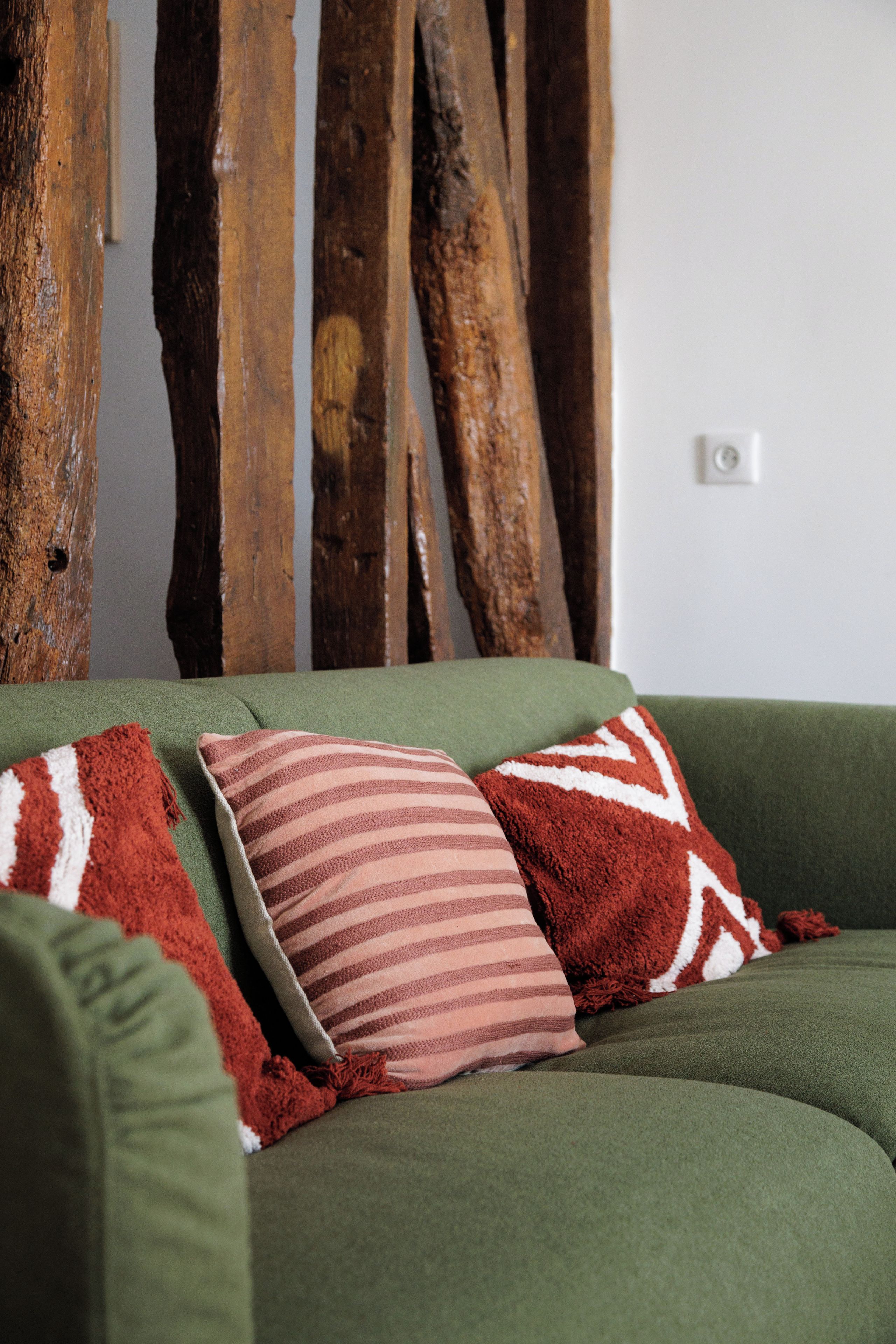 Ein grünes Sofa mit drei Kissen in einem Raum, der eine Holzwand und eine weiße Schalttafel hat.