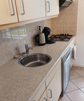 A kitchen with a stainless steel sink, a kettle, and a stove.