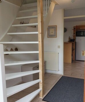 A staircase with white railings leading to a landing. A radiator is mounted on the wall, and a kitchen area is visible in the background. - Holiday home with 2 bedrooms (Medemblik)