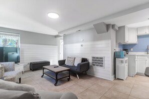 Ein modernes Wohnzimmer mit Flachbildfernseher, einer Couch, einem Couchtisch und einer Küchenzeile mit Schränken und einer blauen Spritzschutzwand.