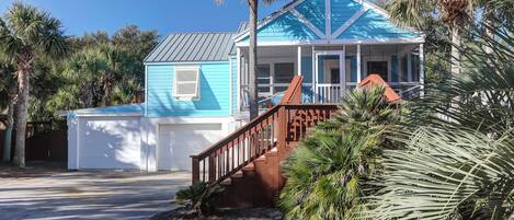 A two-story house with a blue exterior, a covered porch, and a wooden staircase leading to the entrance.