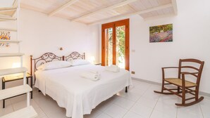 Una camera da letto con un letto, una sedia, un comodino e un quadro appeso al muro.