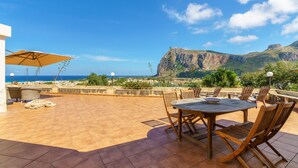 Una terrazza con tavolo e sedie, con vista sulla costa e una montagna sullo sfondo.