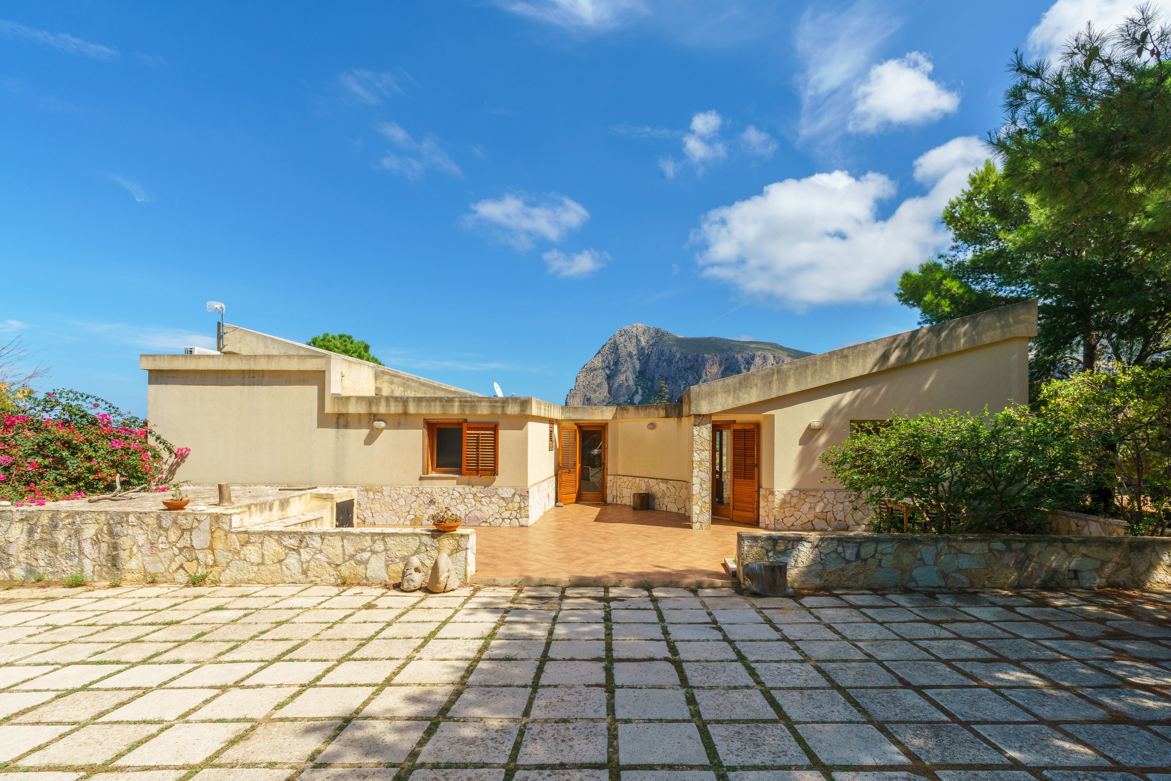 Un bâtiment à deux étages avec une façade en pierre, un patio dallé et une montagne en arrière-plan.