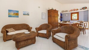 Un soggiorno con mobili in vimini, una zona pranzo con tavolo e sedie in legno, e una cucina con piastrelle blu.