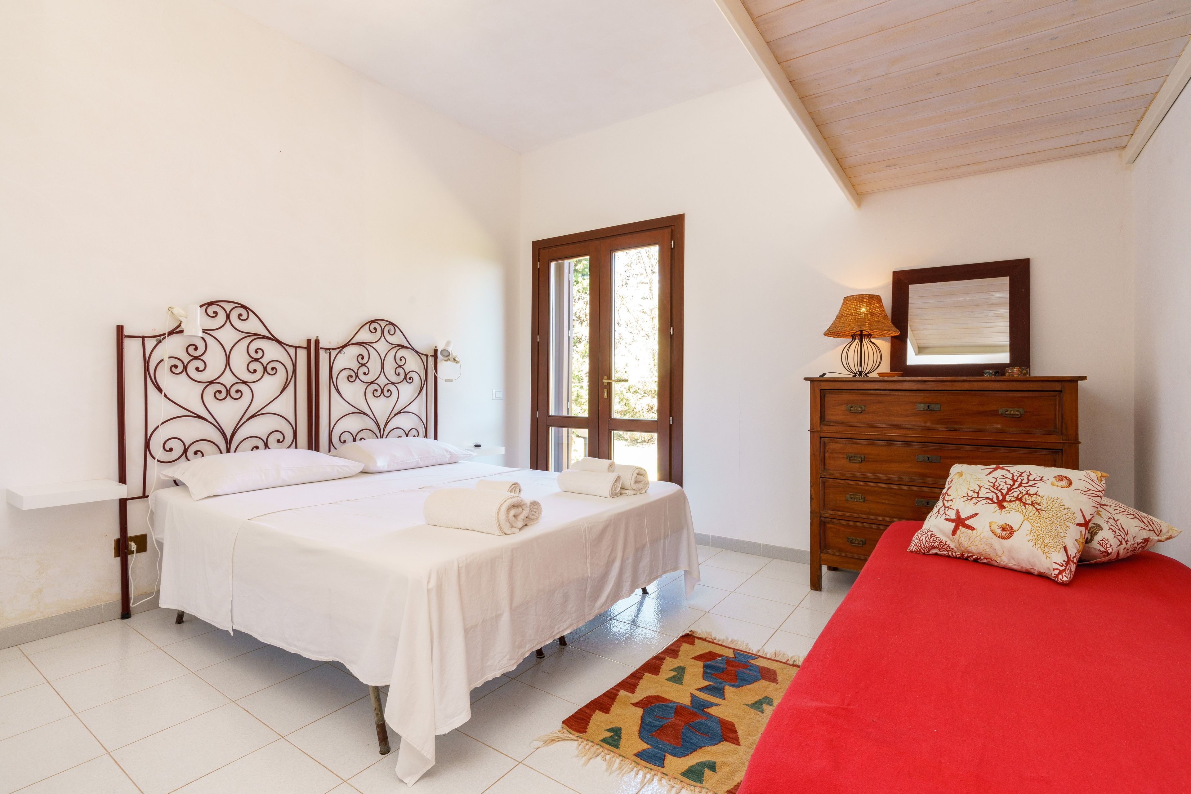 A bedroom with a bed, a dresser, a mirror, and a door leading to a balcony.