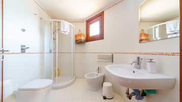 A bathroom with a toilet, bidet, sink, and a glass-enclosed shower.