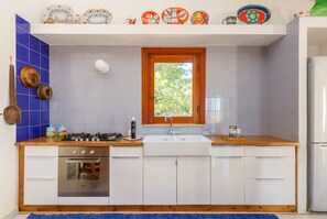 A kitchen with a gas stove, oven, sink, and white cabinets. There is a window with a view of greenery outside.