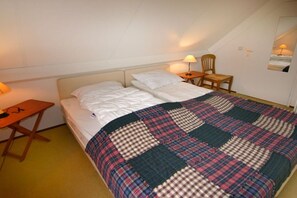Un dormitorio con cama, escritorio, silla y lámpara.
