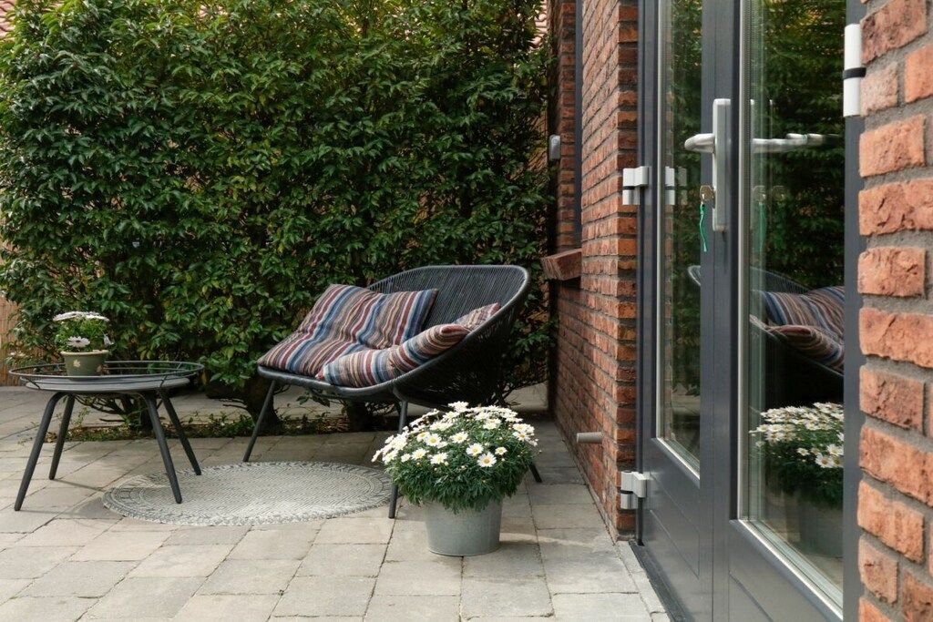 Ein Sitzbereich im Freien mit gepolstertem Stuhl, einem kleinen Tisch und einem Blumentopf.
