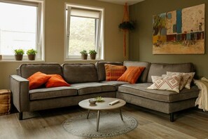 A sectional sofa with multiple cushions, a round coffee table, and a painting on the wall. - Holiday home with 1 bedroom (Oostkapelle)
