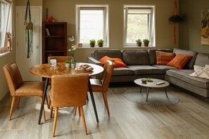 A modern living room with a round dining table, leather sofas, and a bookshelf. - Holiday home with 1 bedroom (Oostkapelle)
