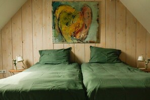 A room with a sloped ceiling and wooden walls, featuring two beds with green bedding and a large abstract painting on the wall. - Holiday home with 1 bedroom (Oostkapelle)