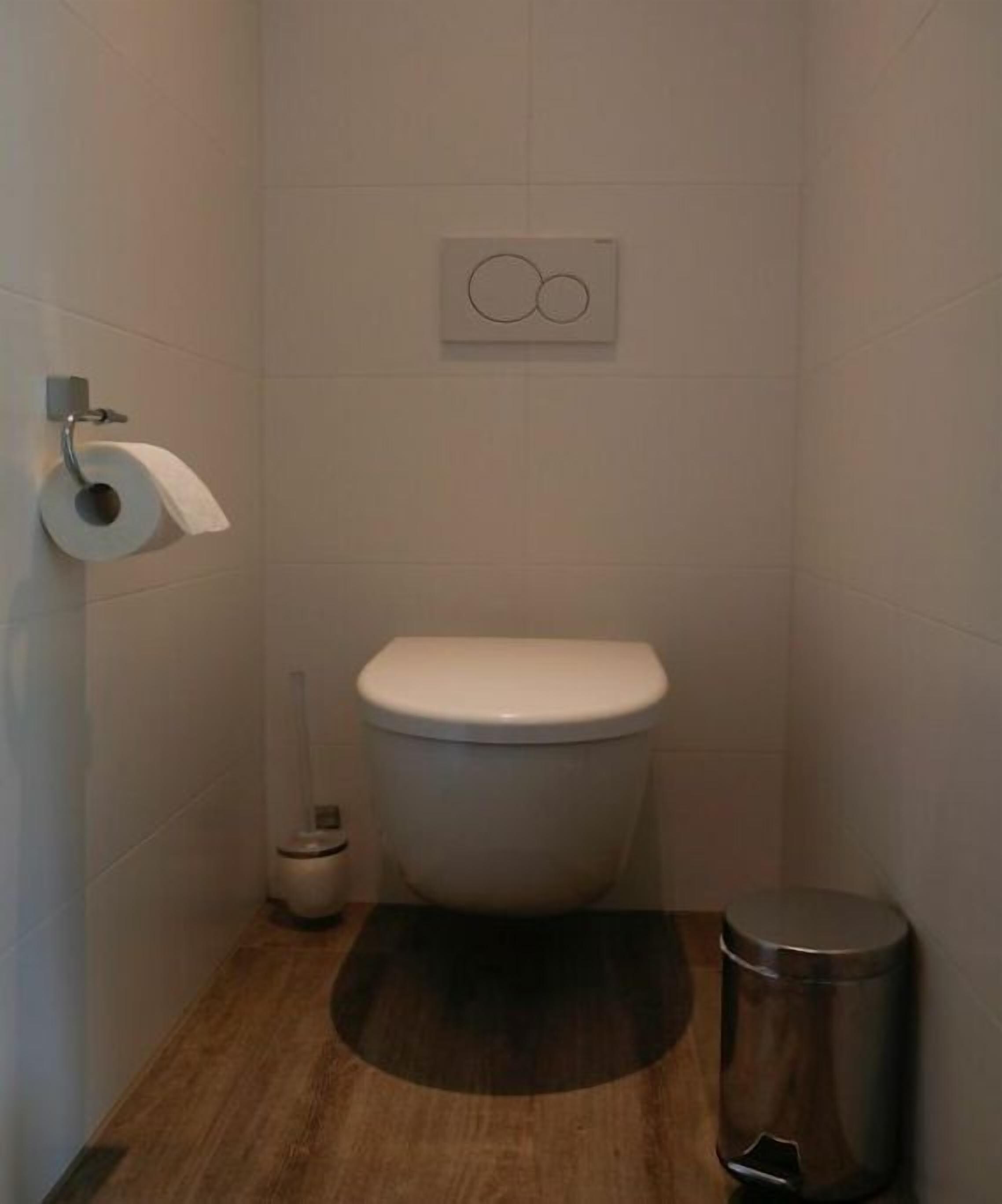 Une petite salle de bain moderne équipée d’un WC, d’un porte-rouleau de papier toilette, d’une poubelle et d’un distributeur de papier toilette fixé au mur.