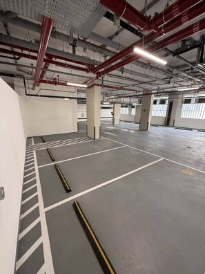 A parking garage with multiple parking spaces, concrete pillars, and overhead pipes. - Central Studio at Hyde Walk   Rooftop Pool & Free Parking (Dubai)