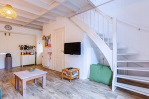 A room with a wooden table, a small shelf with books, a television on the wall, and a staircase. - Holiday home in Veere with swimming pool (Veere)