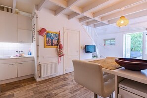 A kitchen with white cabinets, a wooden floor, a dining table with a bowl, and a hanging light fixture. - Holiday home in Veere with swimming pool (Veere)
