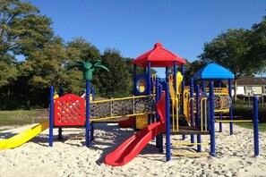 A playground with a red slide, yellow and blue play structures, and a palm tree decoration. - Holiday home in Veere with swimming pool (Veere)