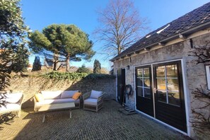 A patio with outdoor furniture, a stone wall, and a building with a tiled roof. - Holiday home in Veere with swimming pool (Veere)