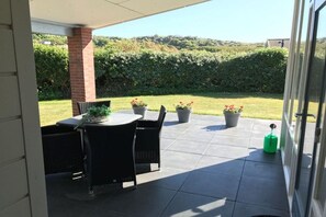 Una zona patio all'aperto con tavolo e sedie, piante in vaso e vista su un paesaggio verdeggiante.