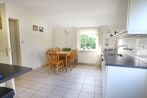 Eine Küche mit Esstisch und Stühlen, ein Fenster mit Blick auf Grünflächen und weißen Schränken.