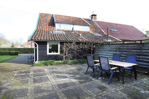 A house with a tiled roof, a wooden deck, and a table with chairs. - Grijpskerkseweg 3 Front (Oostkapelle)