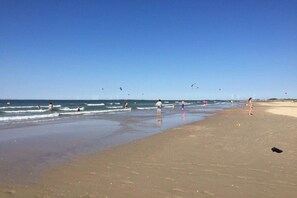 A beach with people swimming and walking, and wind turbines in the distance. - Grijpskerkseweg 3 Front (Oostkapelle)