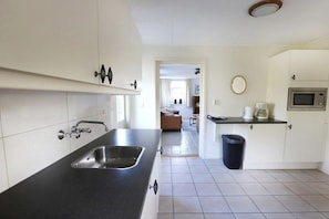 A modern kitchen with a black countertop, stainless steel sink, and white cabinets. - Grijpskerkseweg 3 Front (Oostkapelle)