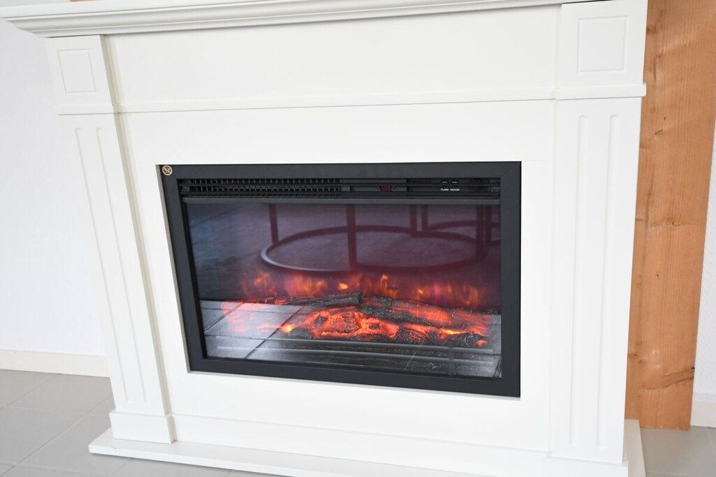 A fireplace with a glass front, a white mantel, and a visible fire.