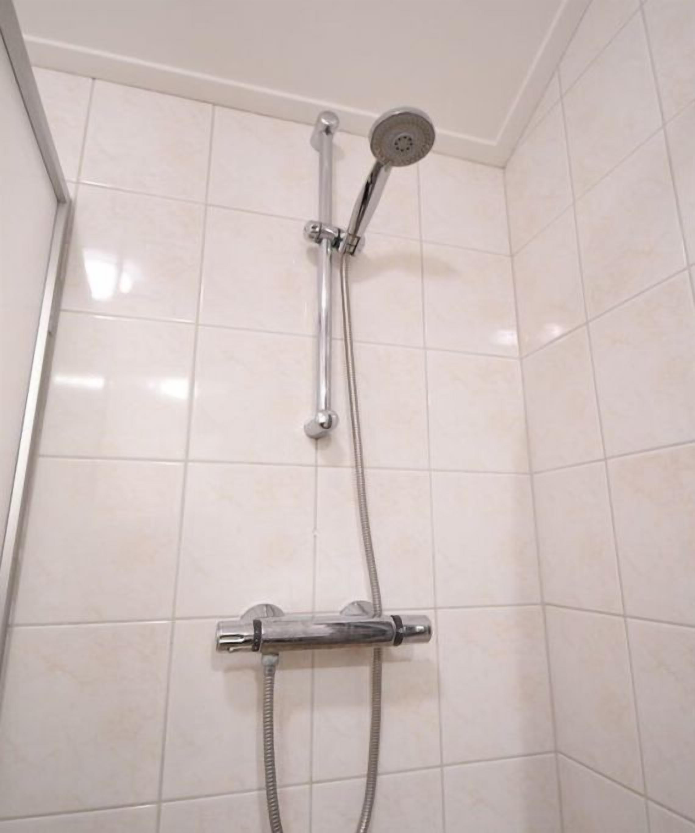 A shower with chrome fixtures and a tiled wall.