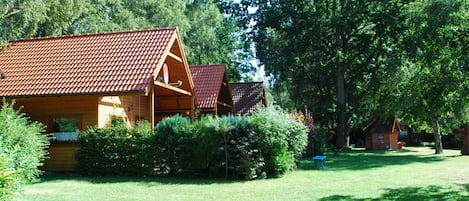 Una cabaña de madera con techo de tejas rojas, rodeada por un césped cuidado y árboles frondosos.