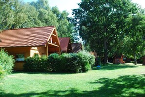 Une cabane en bois avec un toit recouvert de tuiles rouges, entourée d’une pelouse bien entretenue et d’arbres touffus.
