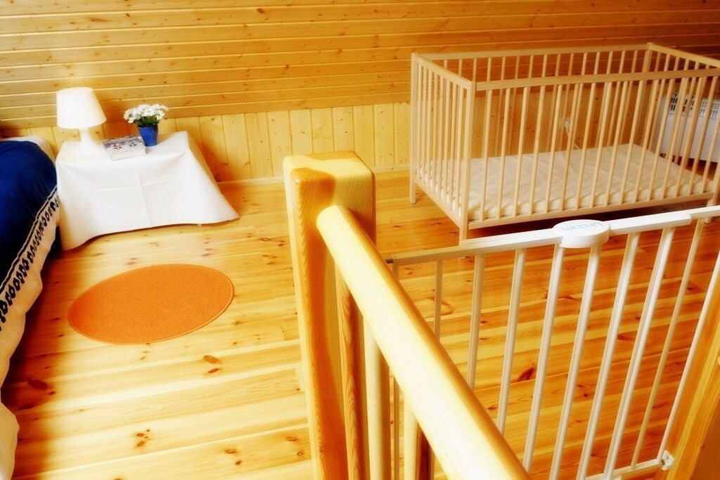 A wooden room with a crib, a small table with a lamp, and a blue pillow.