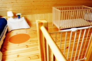 Ein Zimmer mit Holzboden, einem Kinderbettchen, einem kleinen Tisch mit Lampe und einem blauen Kissen.