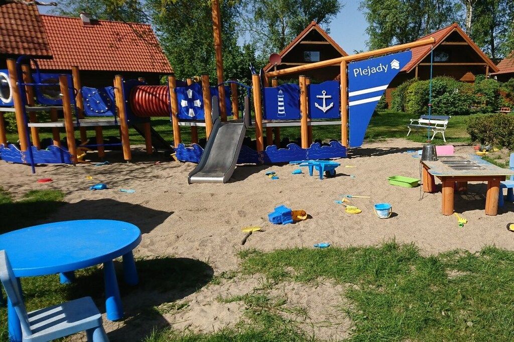 Une aire de jeux au bord de la plage, avec un toboggan, des structures de jeu et une table entourée de chaises.