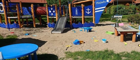 A beachside playground with a slide, play structures, and a table with chairs.