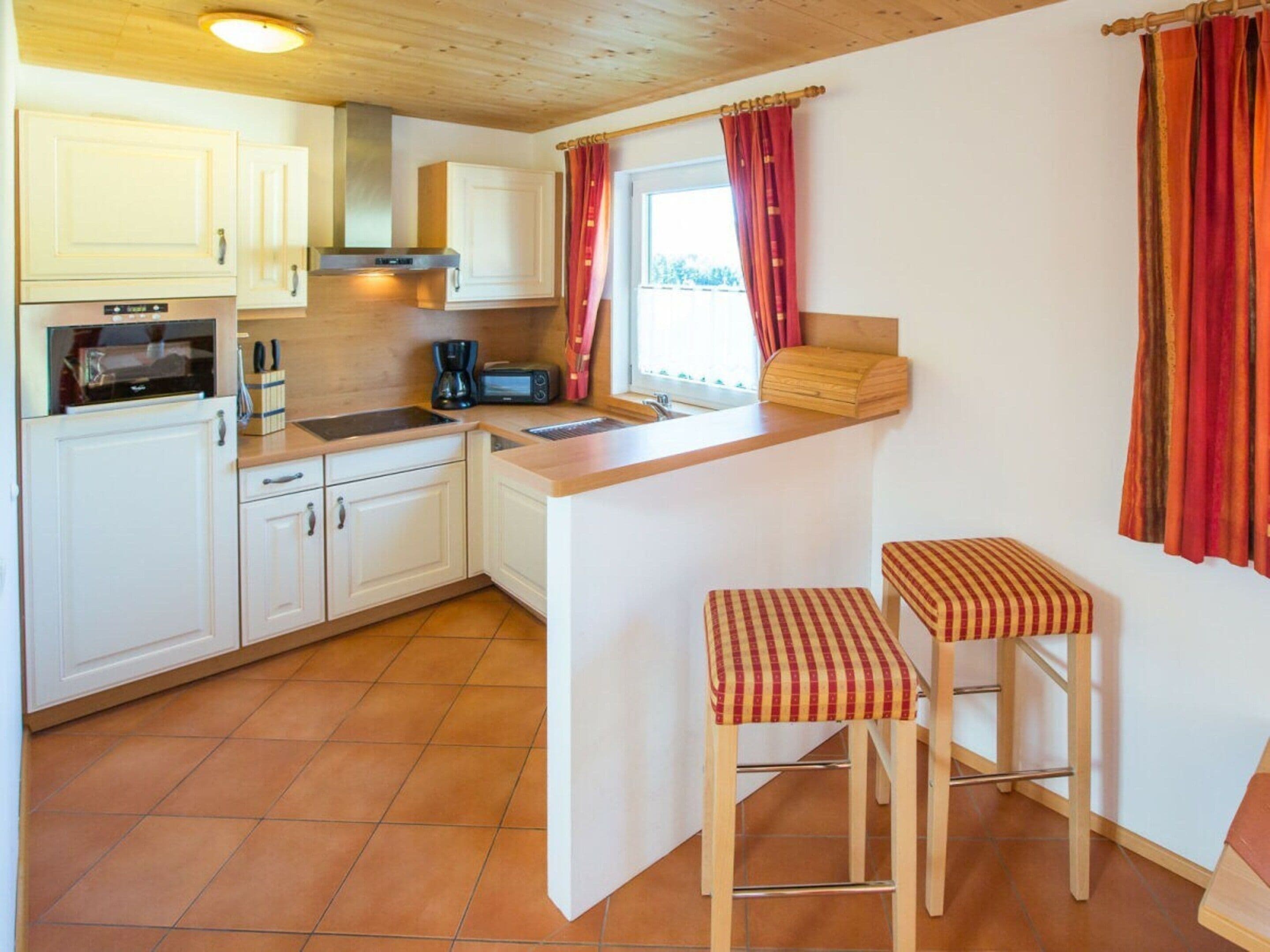 A compact kitchen with white cabinets, a microwave, a coffee maker, and a small island with stools.