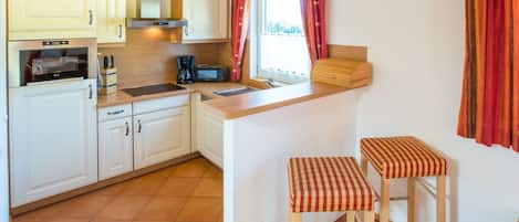 A compact kitchen with white cabinets, a microwave, a coffee maker, and a small island with stools.