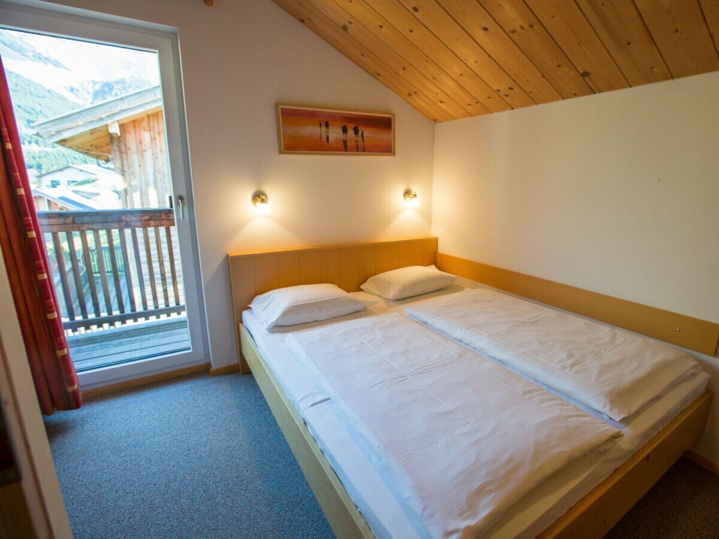 A bedroom with a wooden ceiling, a bed with white bedding, and two wall-mounted lights.