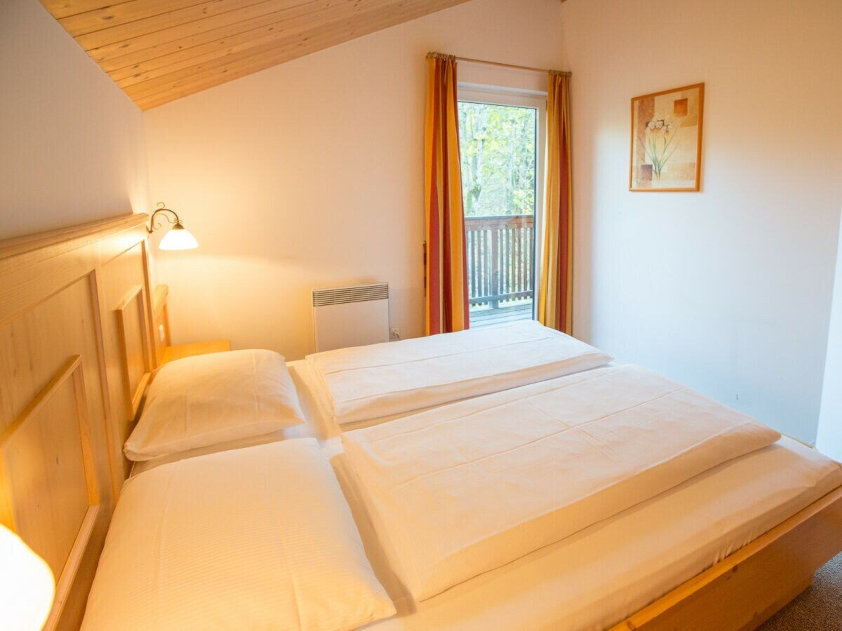 A double bed with a headboard, a bedside lamp, a window with curtains, and a framed picture on the wall.