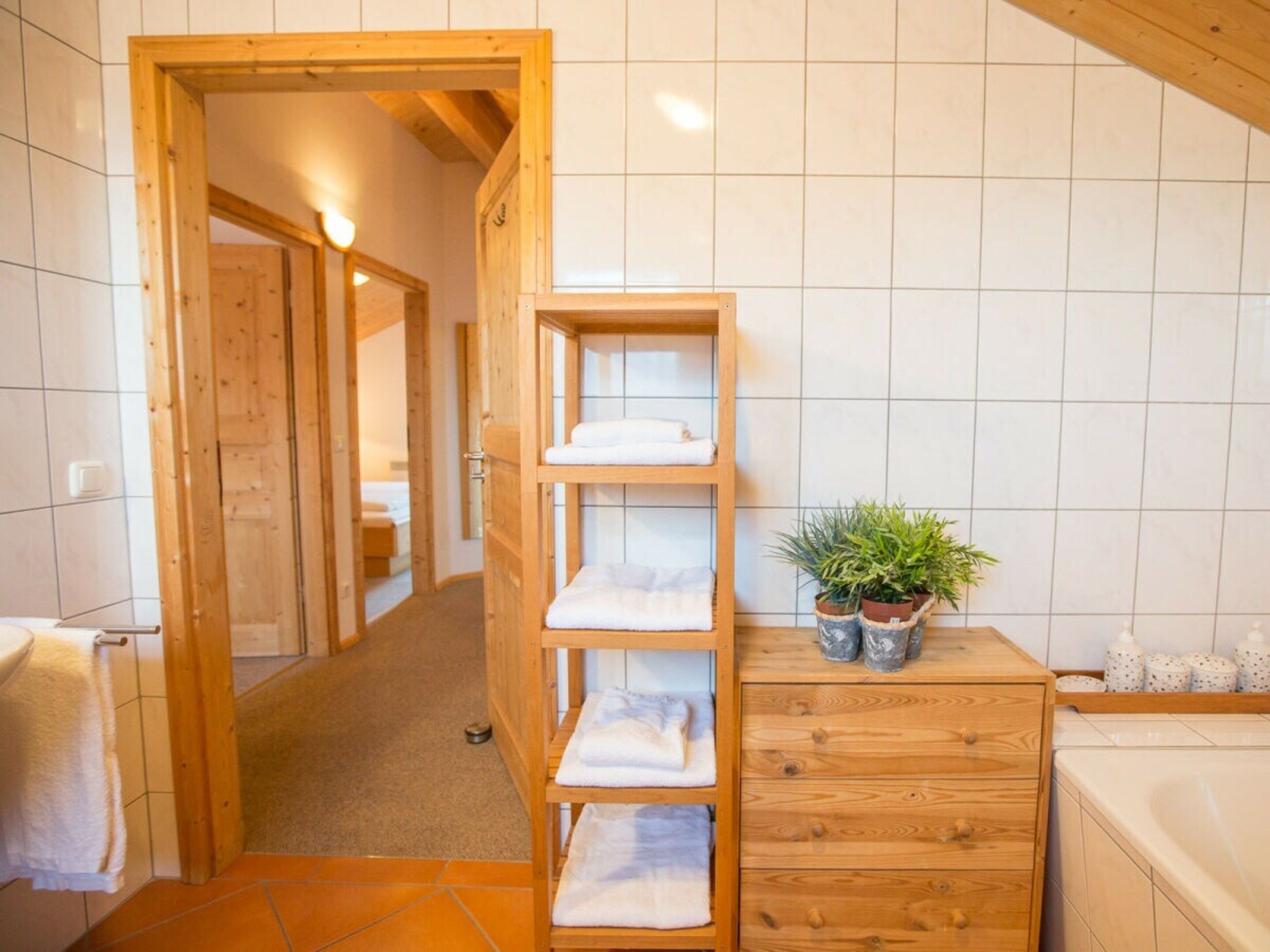 Ein Badezimmer mit Holzregalen, einer Topfpflanze und einer Badewanne.