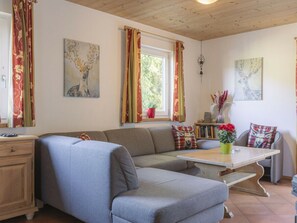 Uma sala de estar aconchegante com sofá seccional, uma mesa de madeira e uma janela com cortinas.