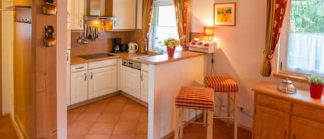 A kitchen with white cabinets, a stove, a coffee maker, and a window with curtains.