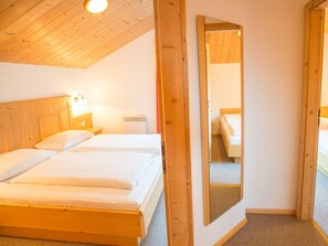 Quarto com cabeceira de madeira, mesa de cabeceira com abajur e um espelho grande na parede.
